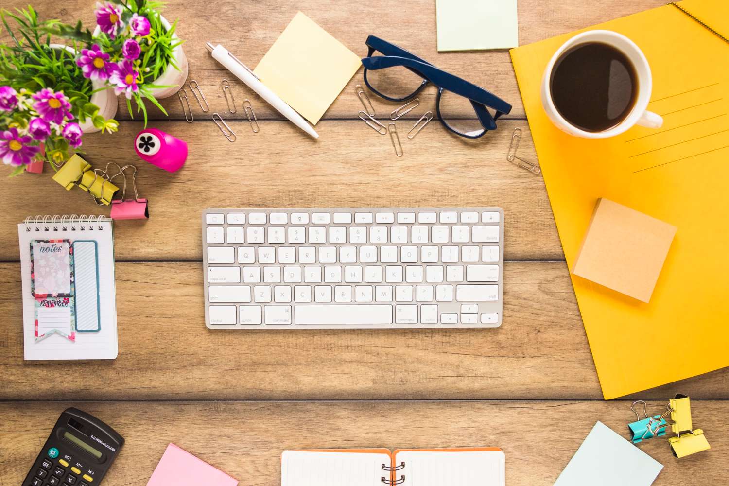 Beautiful desk with keyboard, some flowers, coffee and other stuff.